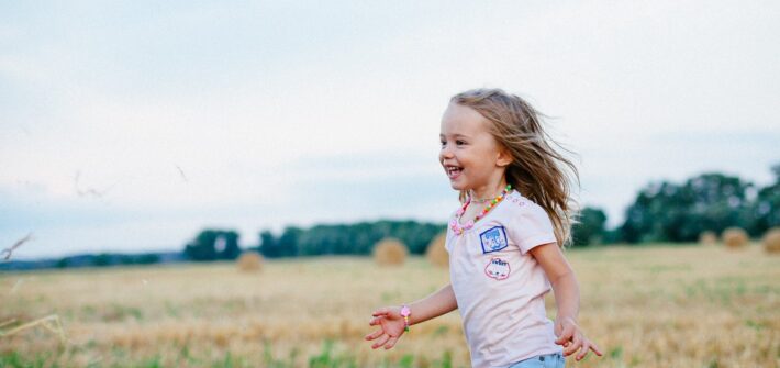 Smiling Girl Running Towards Left on Green Field