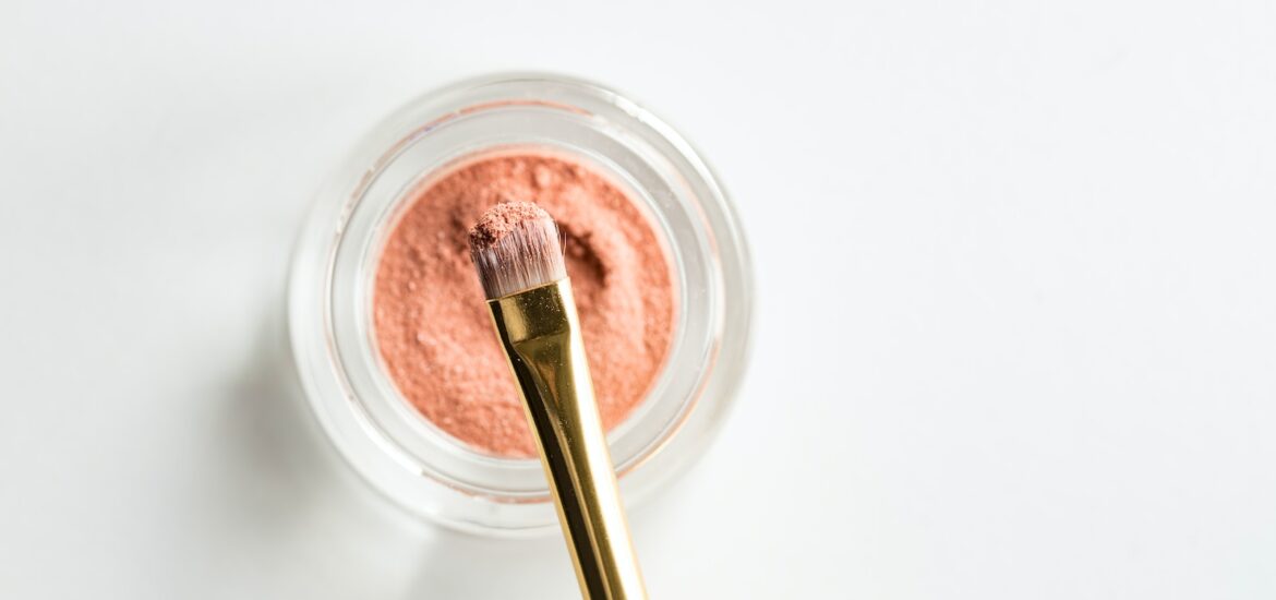 brown makeup brush in front pink powder on glass case